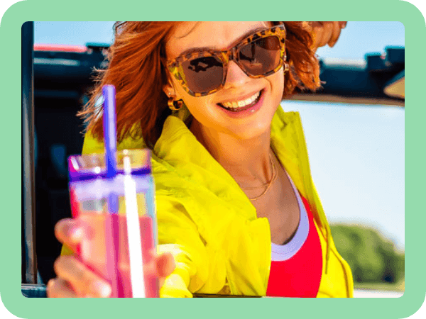 Woman hanging out of the window of a car holding a cup with Harmony mixed in.