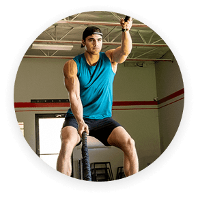 Man in workout clothes using battle ropes in a gym.