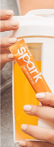 Hands holding a stick pack of Spark Mandarin Orange with a mixed bottle of Spark.