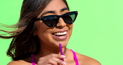 Woman smiling and sipping a drink against a green background.