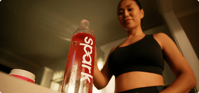 Woman in workout clothes filling a Spark branded water bottle with Fruit Punch spark.