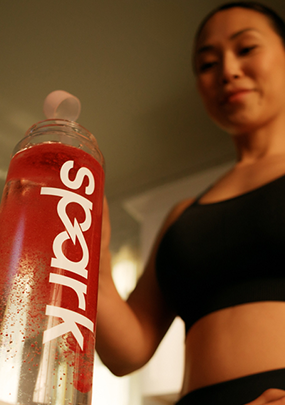 A woman pouring Spark® into a Spark® labeled bottle of water.