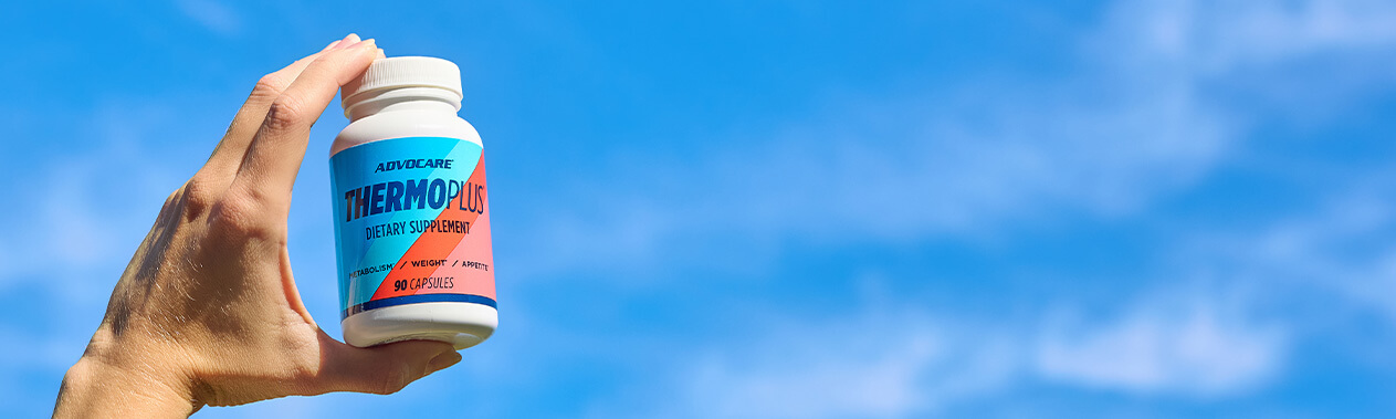 A hand holding up a bottle of ThermoPlus in a bright blue sky.