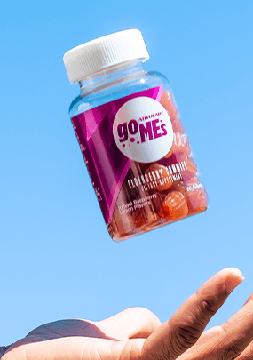 A hand about to catch a bottle of GO MEs Elderberry gummies.