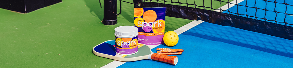 Spark Passion Fruit on top of pickleball rackets on a pickleball court.