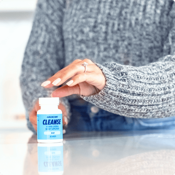 Woman in grey sweater holding a bottle of AdvoCare Cleanse on a white kitchen counter.
